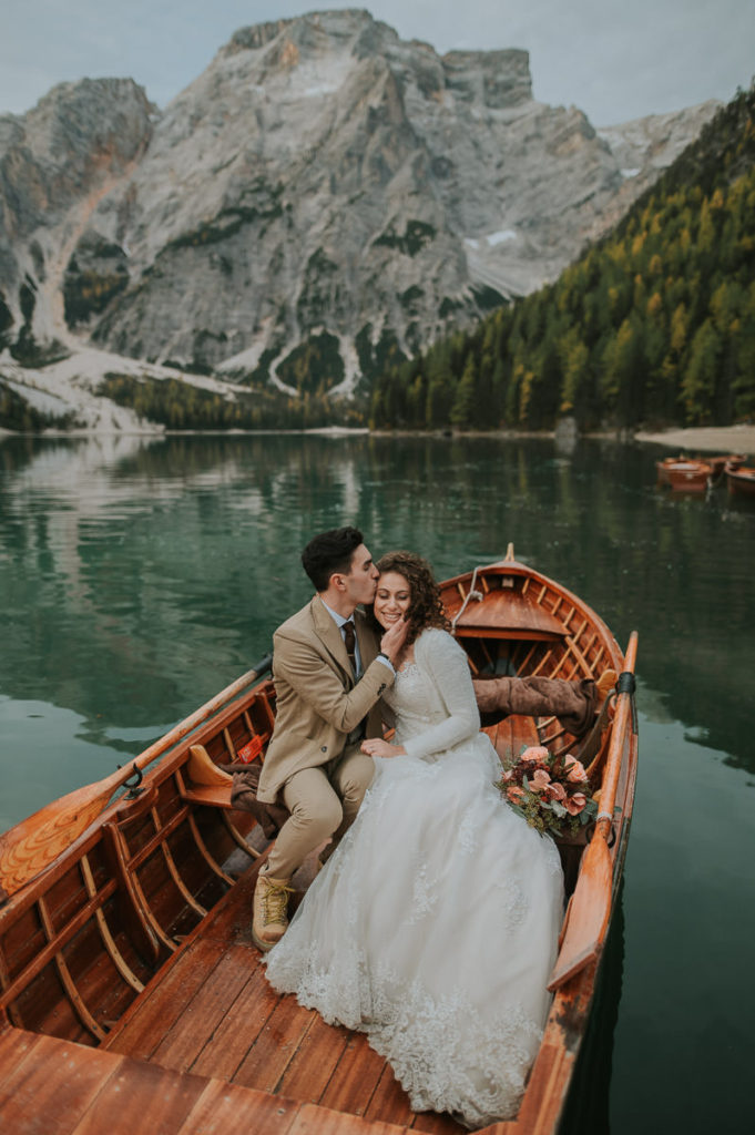 Bride and groom sitting in a wooden boat and kissing on Lago di Braies on the day of their elopement in Italy