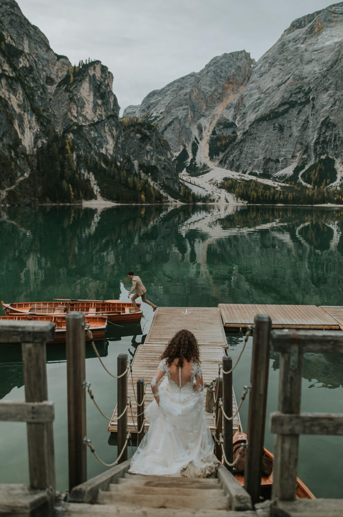 Bride and groom walking towards the boats on a mountain lake in Northern Italy