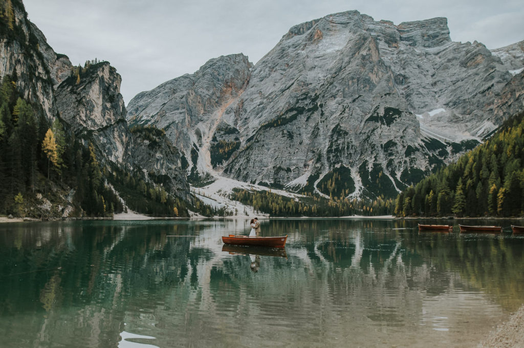 Bride and groom standing in a wooden boat  and kissing in the middle of the Lake Braies in Northern Italy 