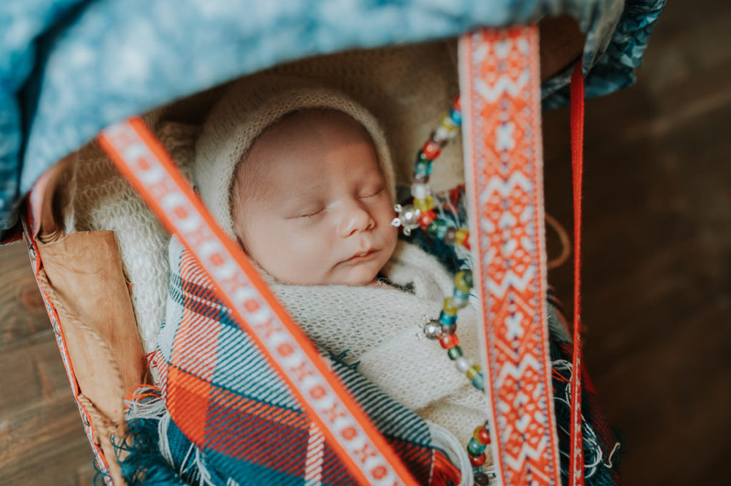 Nyfødtfoto av en samisk baby som ligger i en håndlaget komsa 