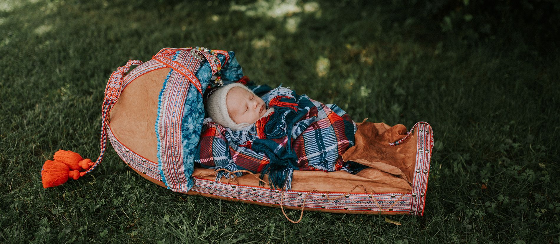 Skjønn nyfødt samisk baby ligger søt i en komsa utendørs i en grønn hage i Alta
