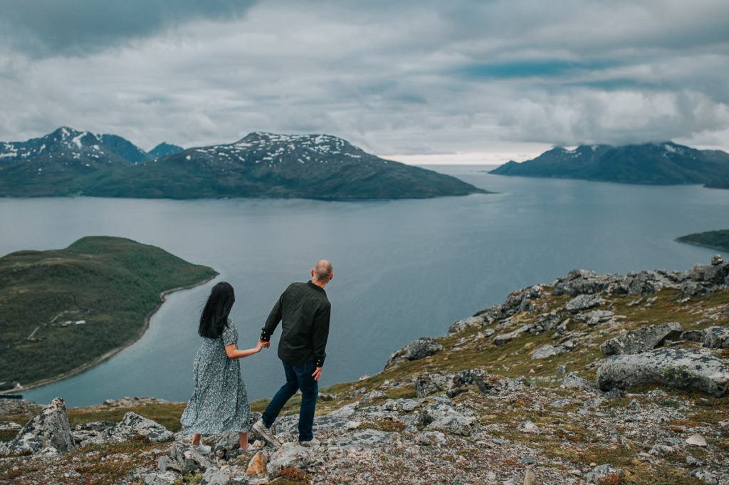 A couple hiking in the mountains  and holding hands, they are facing a great view to Ersfjord in Tromsø