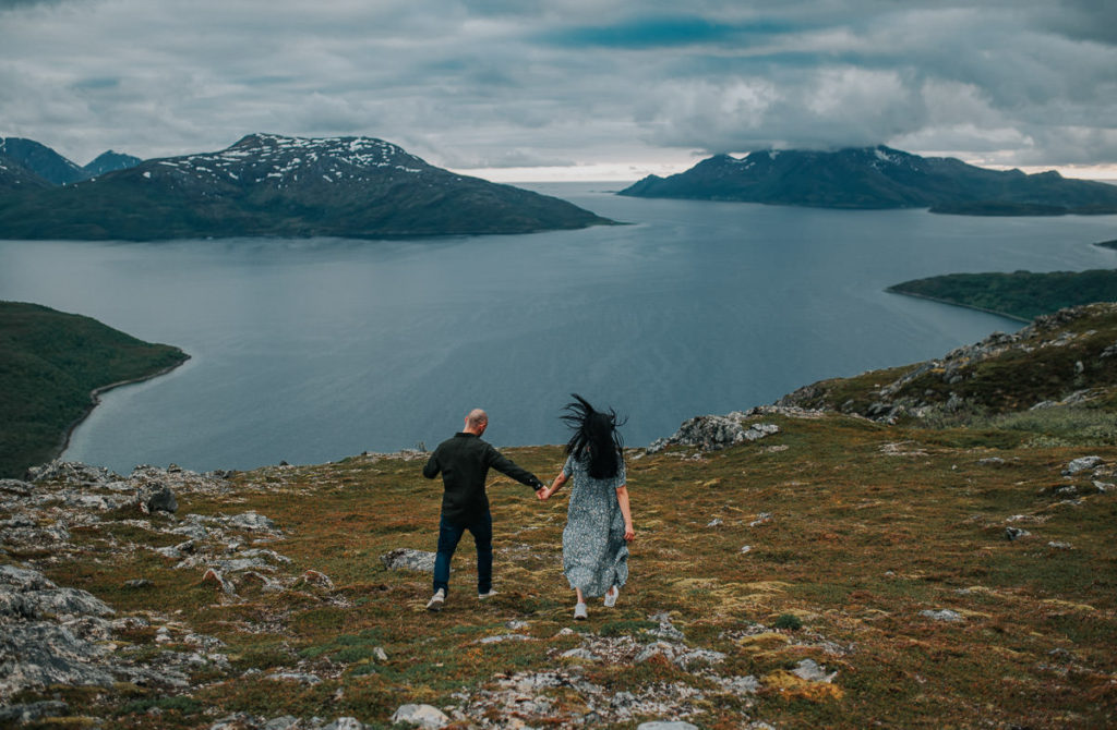A couple hiking in the mountains  and holding hands, they are facing a great view to Ersfjord in Tromsø