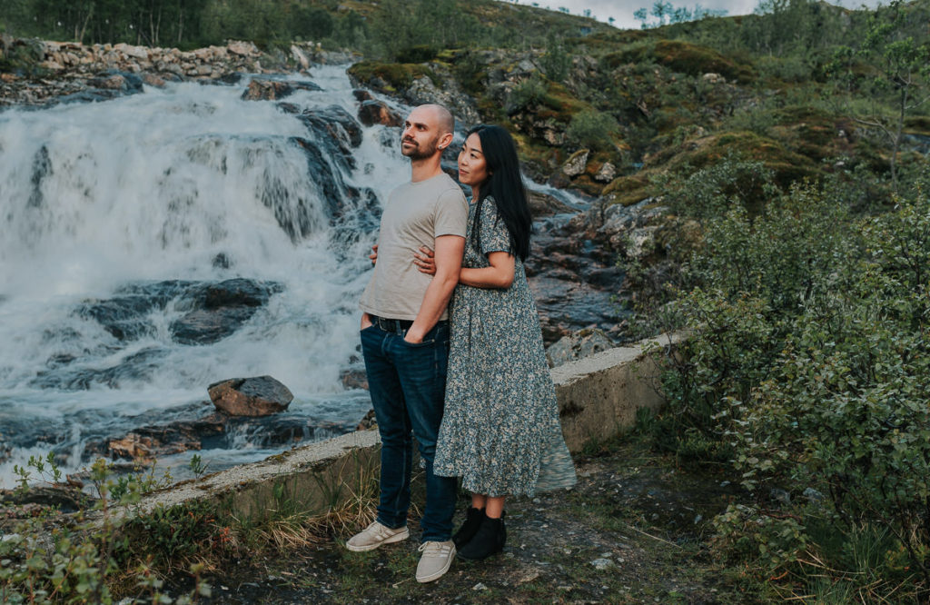 A couple in front of a beautiful waterfall in Tromsø hugging and enjoying the view