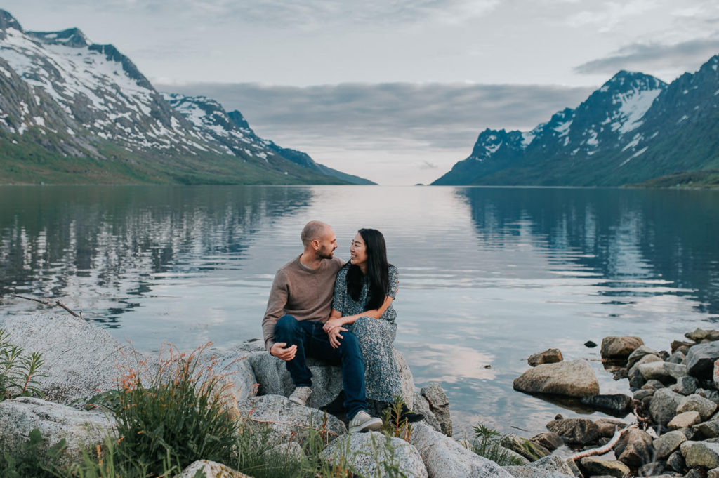 A beautiful couple sitting on the rocks by the fjord Ersfjord in Tromsø on the day of their engagement photo session - by Norway elopement  photographer TS Foto Design