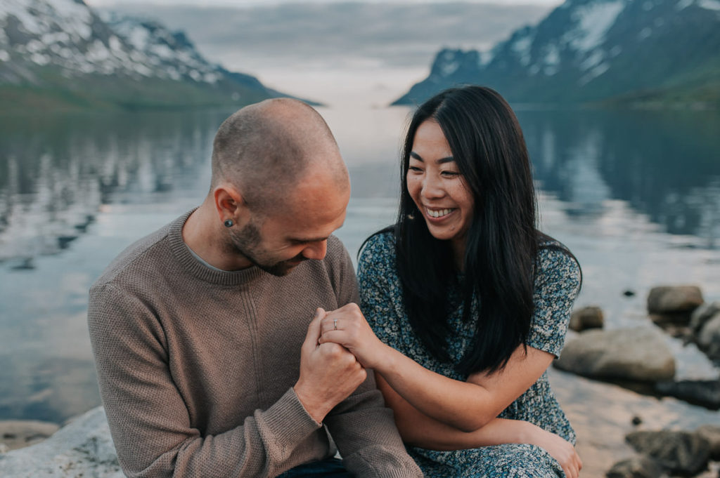 A beautiful couple sitting on the rocks by the fjord Ersfjord in Tromsø on the day of their engagement photo session - by Norway elopement  photographer TS Foto Design