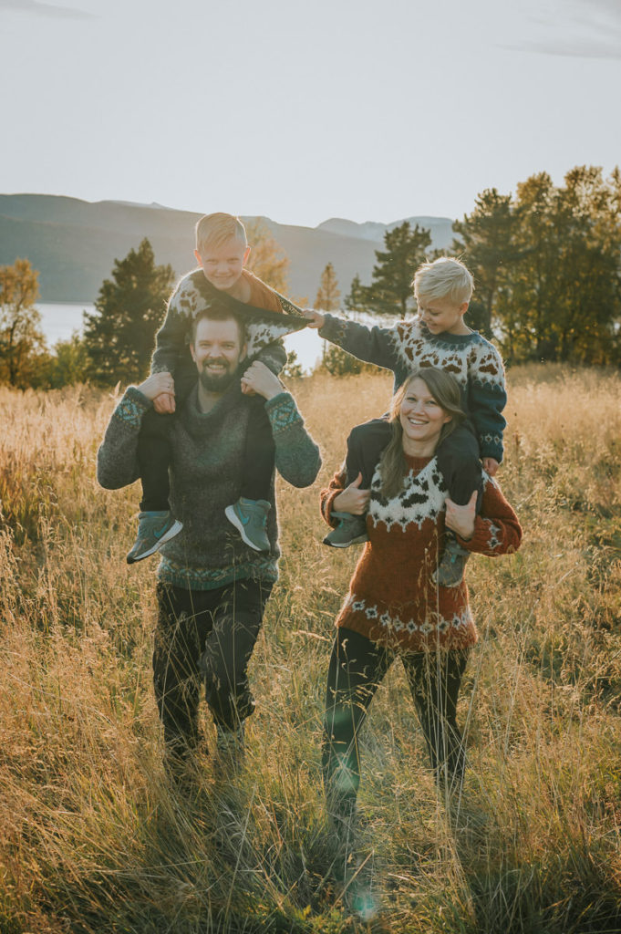En familie på fire spaserer i et stråfelt mens de holder sønnene sine på skuldre. Det er en fin høstdag under en solnedgang utenfor Alta i Finnmark
