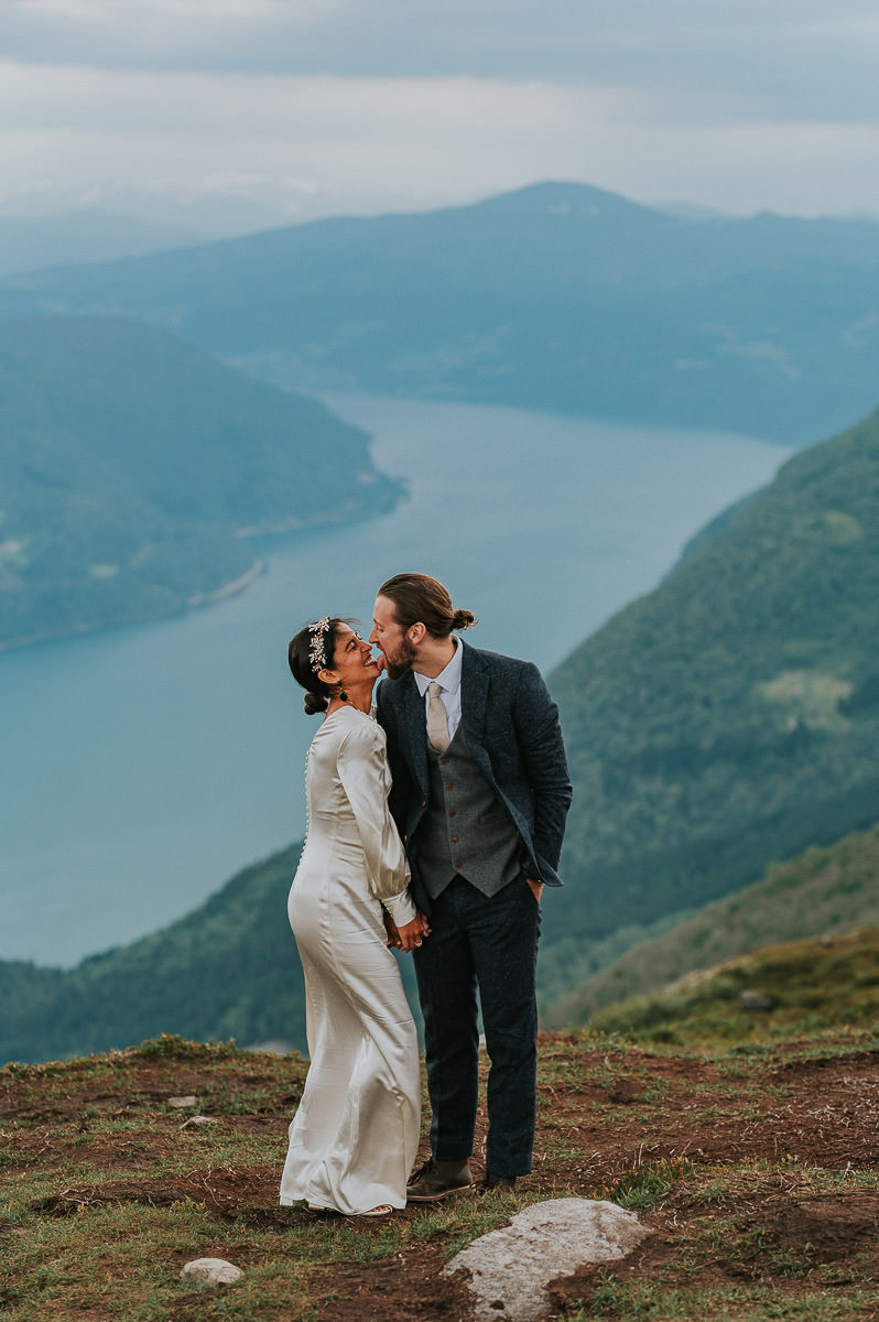 Bride and groom having a funny moment when the groom licks the bride on the chick on a mountaintop in Loen Western Norway on the day of their elopement