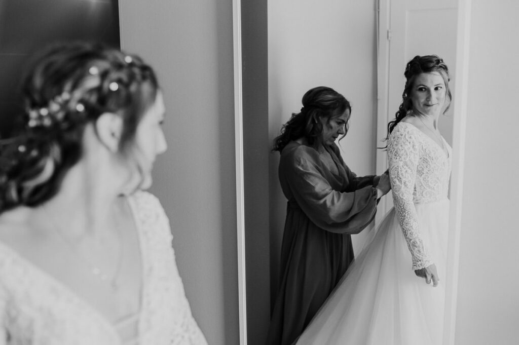 Beautiful bride getting ready for her winter wedding ceremony - maid of honor helping her to put on her wedding gown