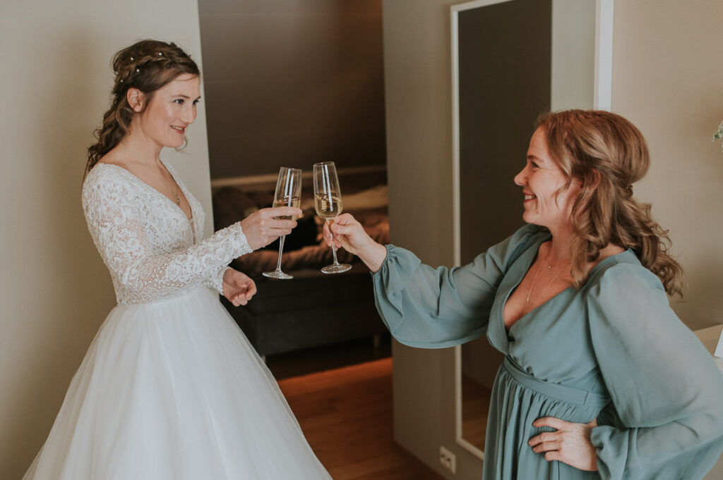 Bride in a beautiful longsleeve lace dress and her maid of honor cheering with the champagne glasses before their wedding ceremony in an igloo hotel in Alta Norway