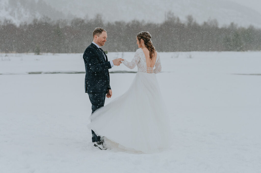 Bride and groom dancing outdoors  in front of white  winter landcape in Alta Northern Norway under a beautiful blizzard snowfall right before their dogsledding winter wedding ceremony in Norway