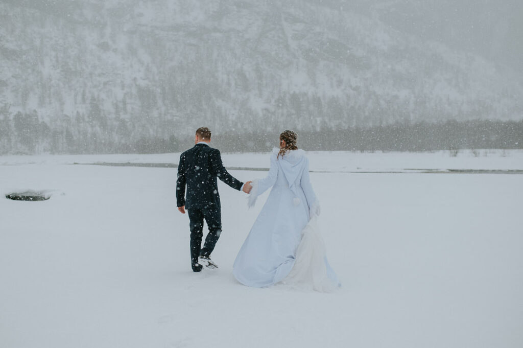 Bride and groom walking into a  white winter landscape in Alta Northern Norway under a beautiful blizzard snowfall 