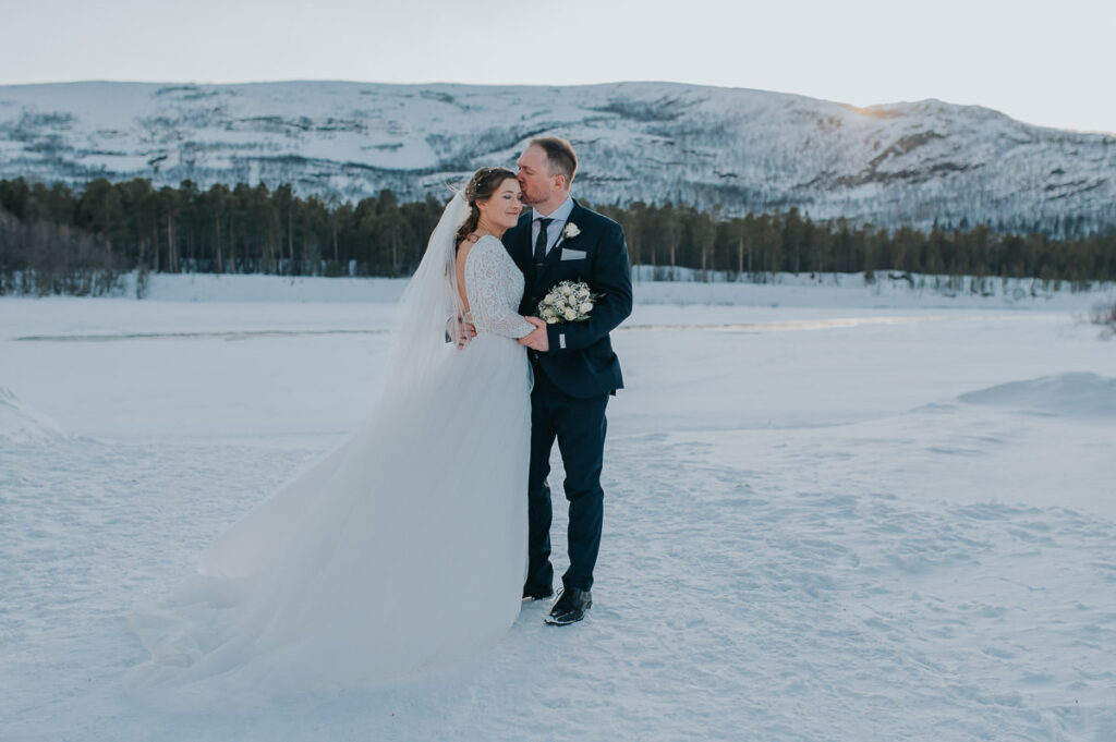 Portraits of the bride and groom and on the day of their winter wedding in Alta Norway among beautiful winter landscapes with mountains, river and the winter sun