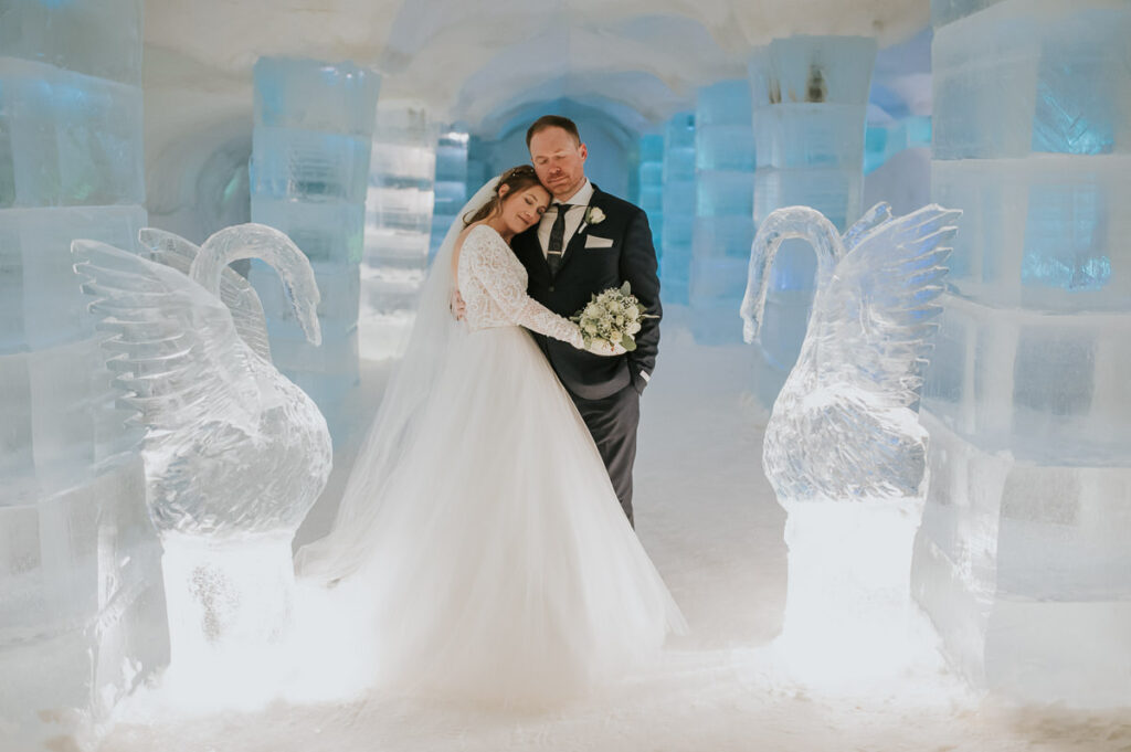 Bride and groom hugging and smiling in the igloo hotel ice hotel among ice and snow sculptures after their winter wedding ceremony in Sorrisniva Alta Norway
