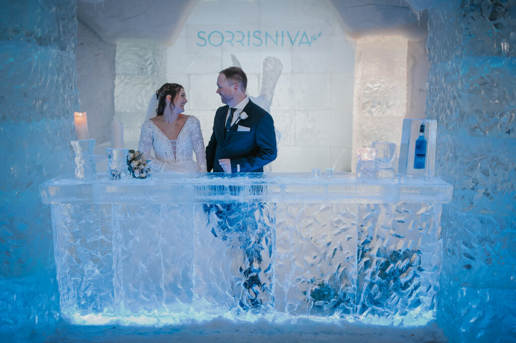 Bride and groom hugging and smiling in the igloo hotel ice hotel among ice and snow sculptures after their winter wedding ceremony in Sorrisniva Alta Norway