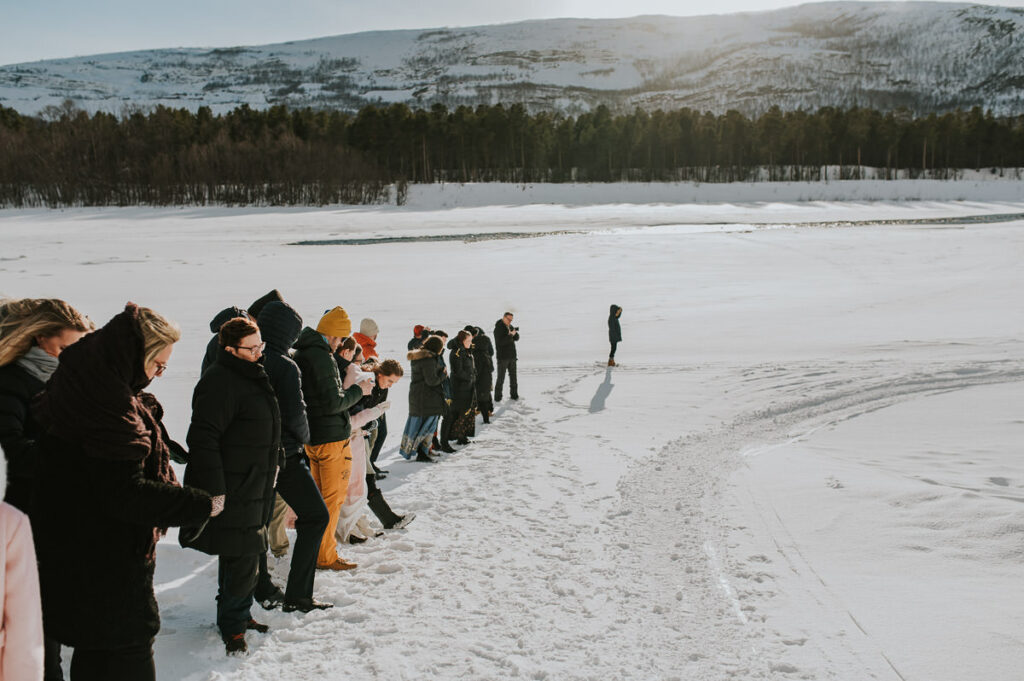Wedding guests standing outside in front of a nice winter landscape waiting for the bride and groom to arrive to their winter wedding venue in Norway