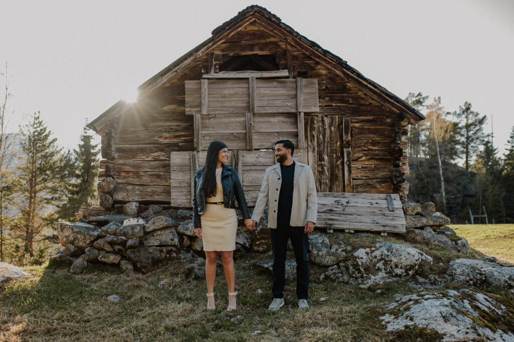 Happy couple holding hands and posing in front of an old hut in the mountains of Aurland