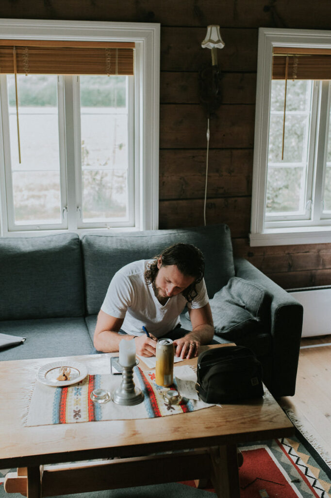 Groom writing his elopement vow on a piece of paper on the morning of elopement day in a cozy cabin