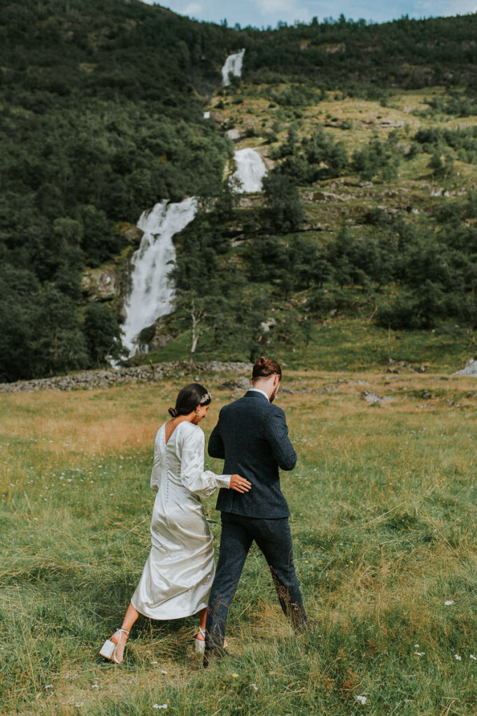 Bride and groom walking towards a stunning waterfall in Loen, Norway