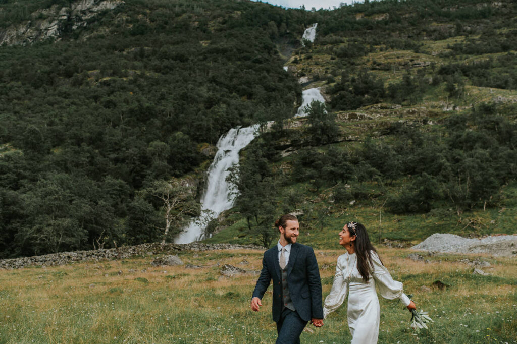Bride and groom walking by the stunning waterfall in Loen, Norway on the day of their elopement