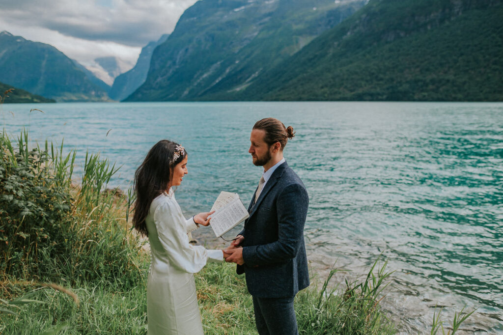 Intimate elopement ceremony by the lake Lovatnet in Loen, Western Norway. The bride is reading her vow from the vow book and groom is drying up some tears