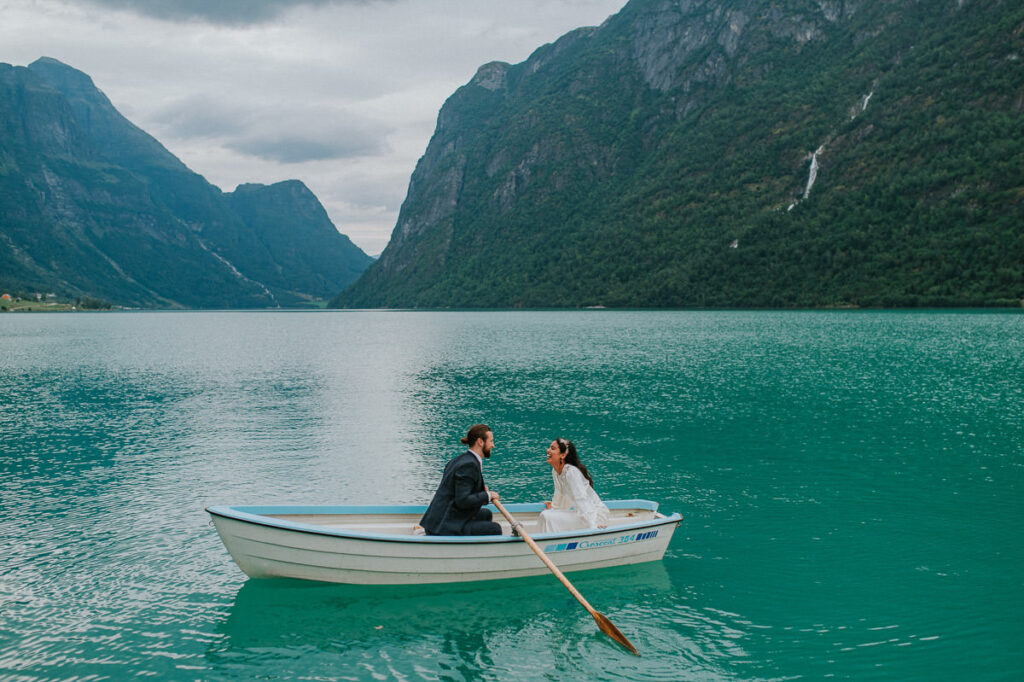 Bride and groom rowing a boat on a gorgeous blue lake Oldevatnet in Loen Stryn Western Norway on the day of their elopement