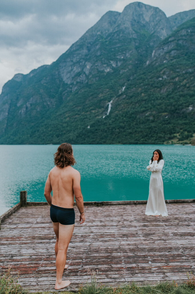 A groom in his underwear ready to jump in a beautiful glacier lake in Loen while bride is watching him, happening on the day of their elopement after the ceremony and other adventures