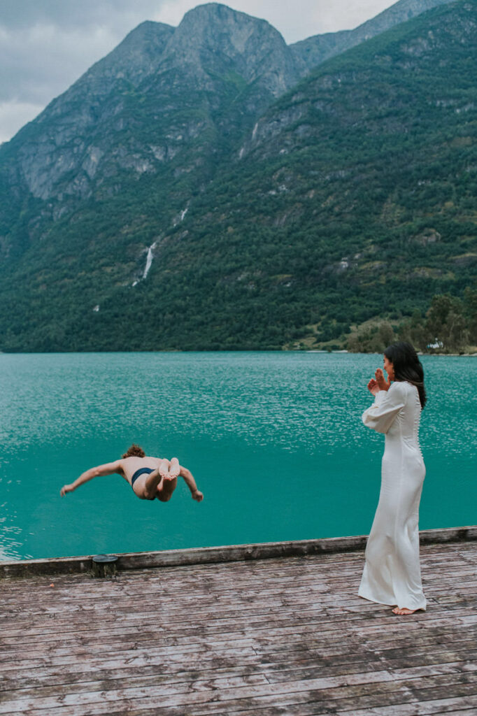 A groom in his underwear is jumping in a beautiful glacier lake in Loen while bride is watching him, happening on the day of their elopement after the ceremony and other adventures