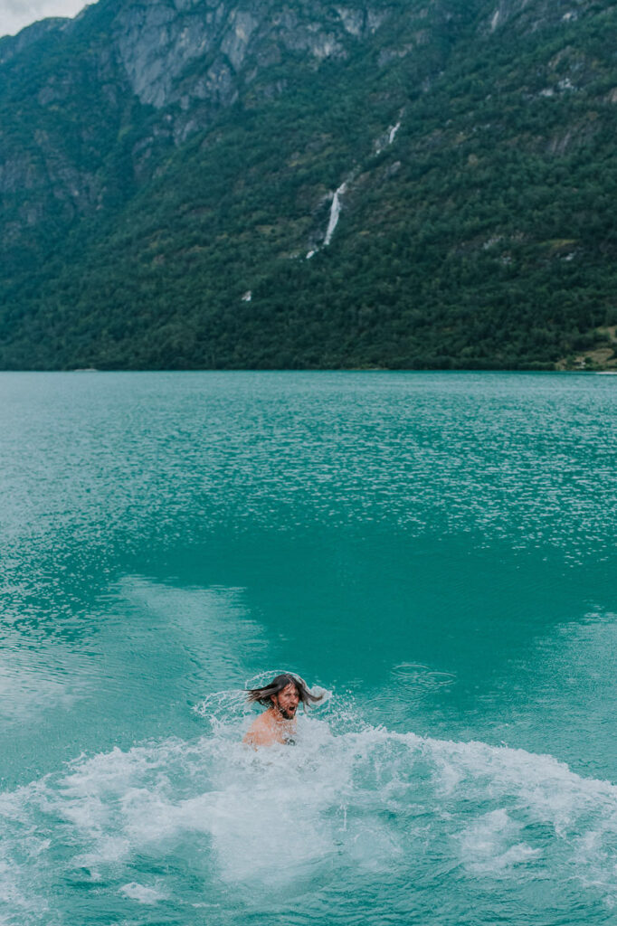 A groom swimming in a beautiful blue lake Oldevatnet on the day of their adventure wedding in Norway