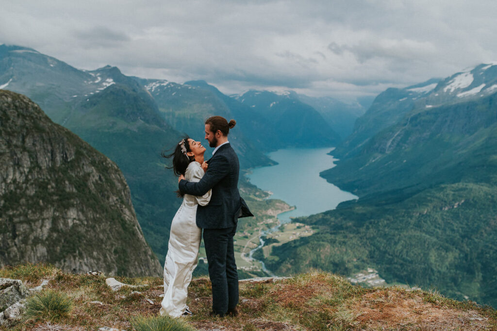 Bride and groom hugging each other in front of a gorgeous view to Lovatnet lake and fjord of Western Norway on the day of their adventure elopement in Loen