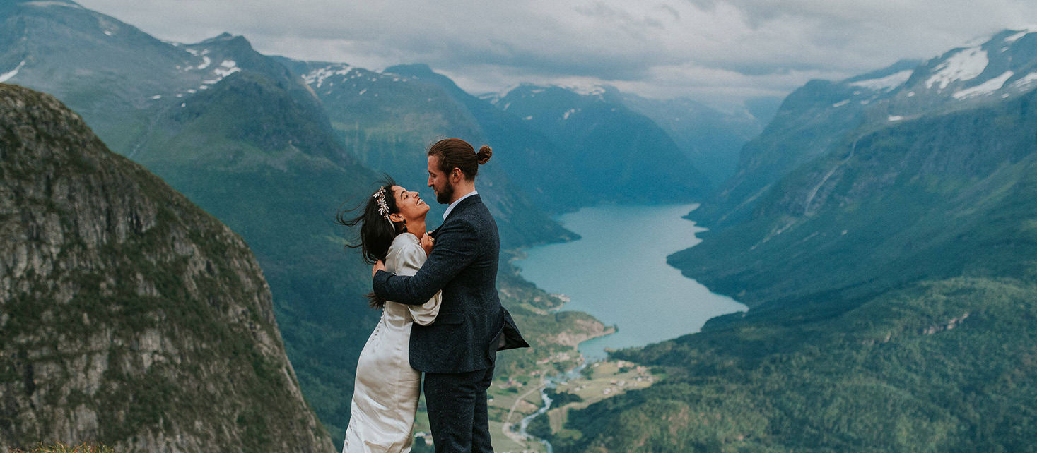 Mountaintop elopement in Loen Western Norway - bride and groom standing on a mountaintop on a windy summer day and laughing