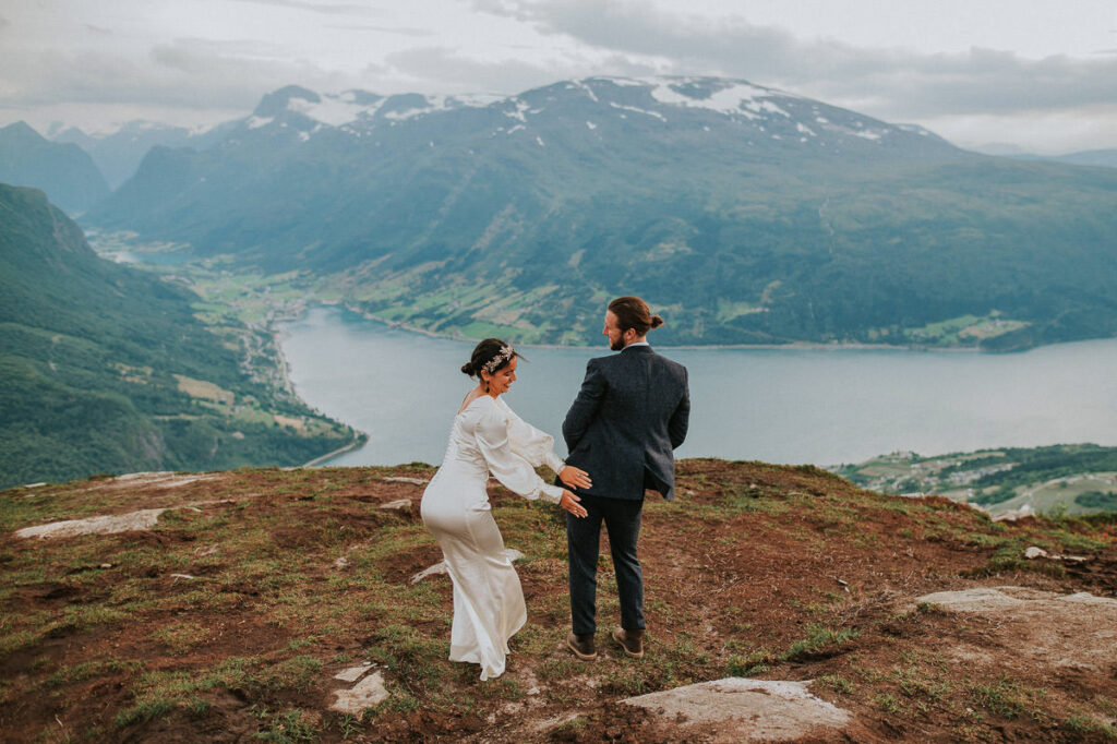 Bridal couple fooling around outdoors in the mountains on the day of their elopement in Western Norway with a gorgeous view to the fjords and mountains