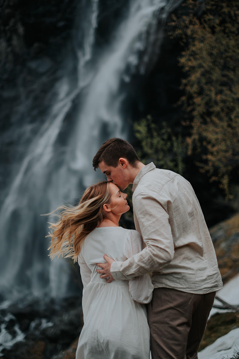 Gorgeous couple kissing in front of a waterfall on their engagement photo session in Alta Norway