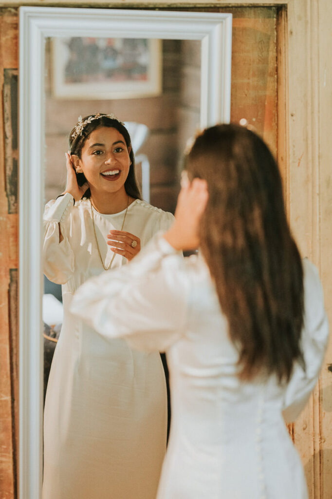 Beautiful bride in a long sleeved ivory wedding dress taking a look in the mirror before her elopement ceremony