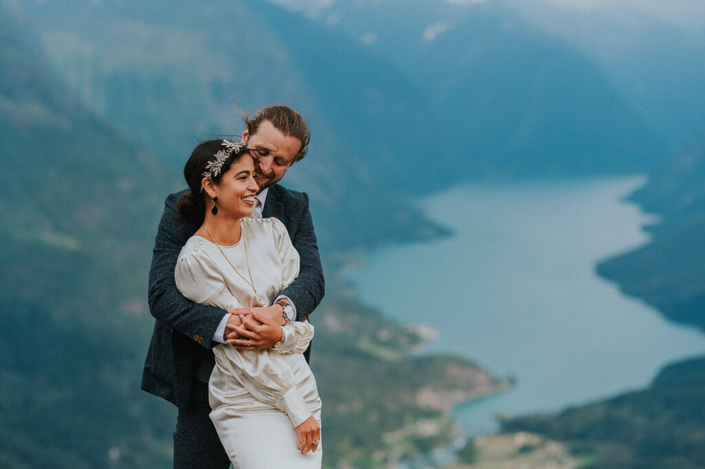 Bride and groom hugging each other in front of a gorgeous view to Lovatnet glacier lake and fjord of Western Norway on the day of their adventure elopement