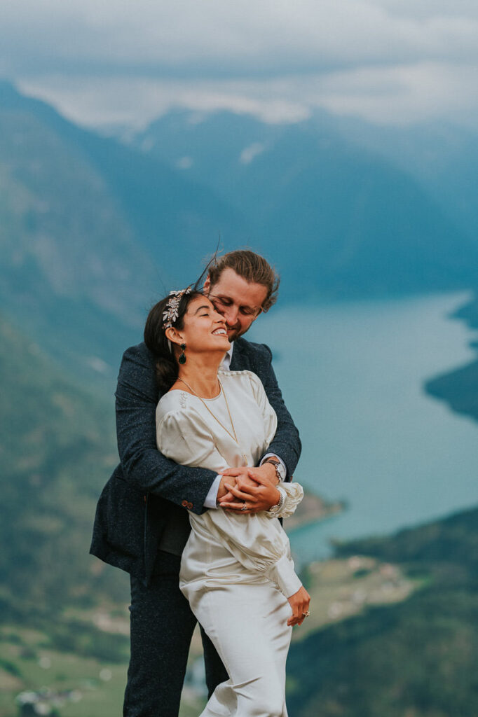 Bride and groom hugging each other in front of a gorgeous view to Lovatnet lake and fjords of Western Norway on the day of their adventure elopement