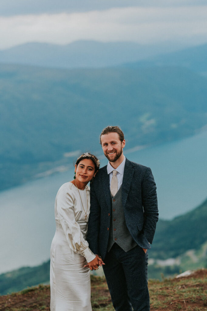 Bride and groom smiling to the camera standing on a mountaintop on the day of their elopement in Loen Norway