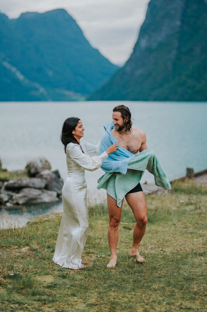 A groom jumped in the lake in Loen at the end of their elopement day and bride is helping him to get dry after the swimming