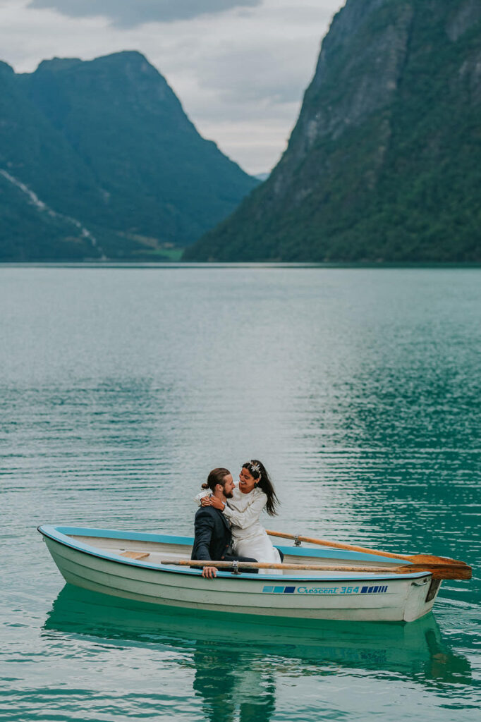 Bride and groom rowing a boat on a gorgeous blue lake Oldevatnet in Stryn Western Norway after their wedding  ceremony on lake Lovatent