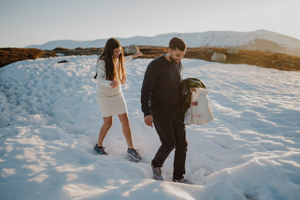 A guy and a girl walking through the snow in the mountains in the sunset