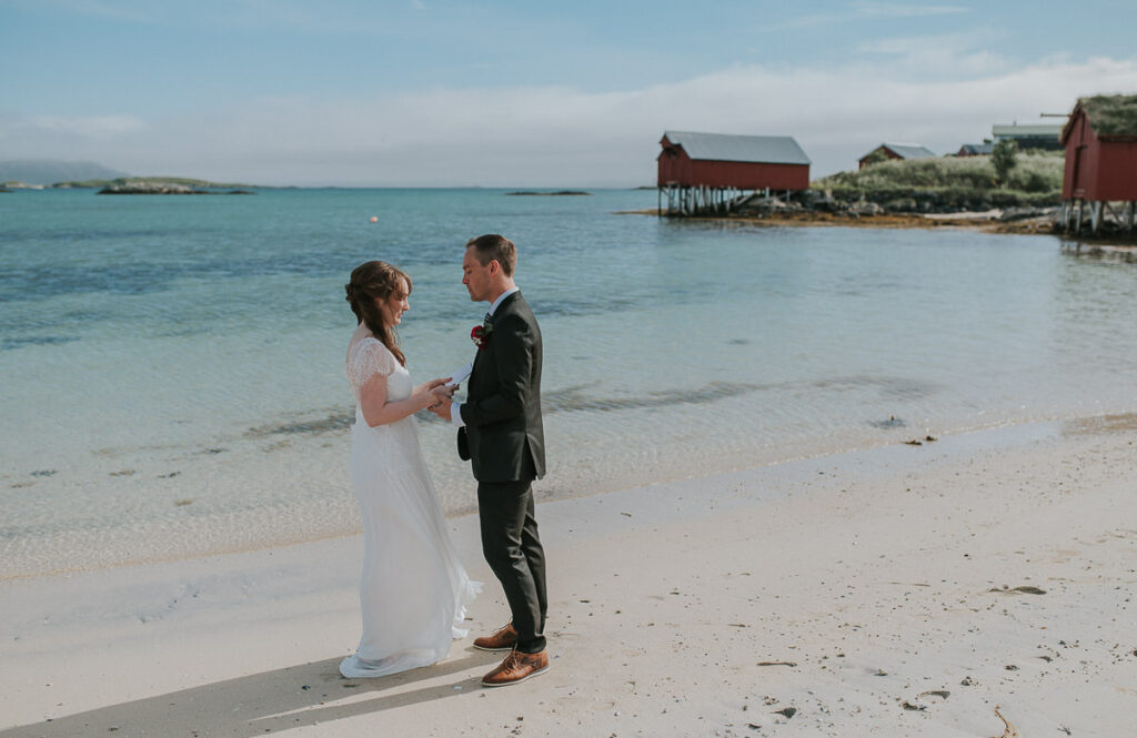 Elopement ceremony on a beautiful beach in Sommarøy island outside of Tromsø. Bride and groom reading their handwritten vows to each other in front of turquoise sea 