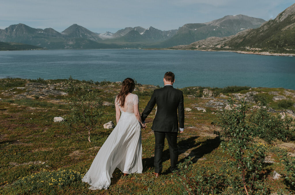 Bride and groom walking on Sommarøy island and enjoying beautiful day and mountain views
