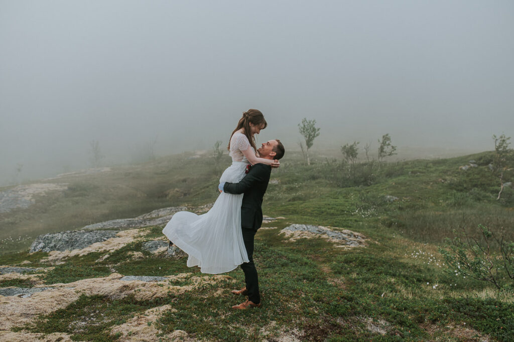 Beautiful bridal couple wandering in a fog in Senja island of Northern Norway on the day of their summer elopement 