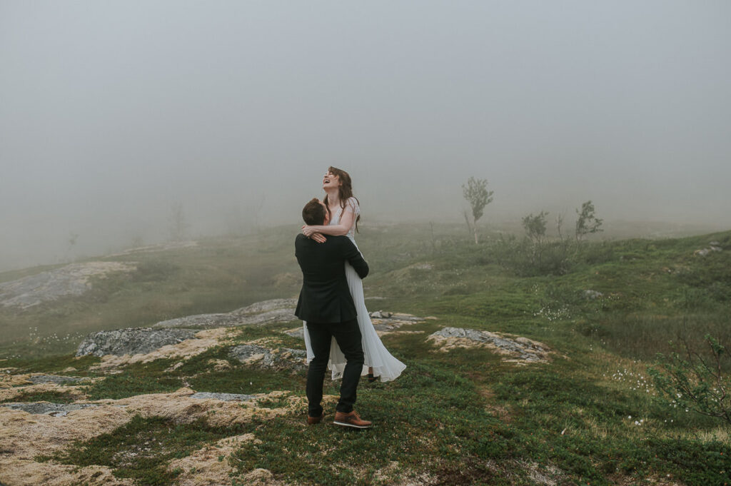 Beautiful bridal couple wandering in a fog in Senja island of Northern Norway on the day of their summer elopement 