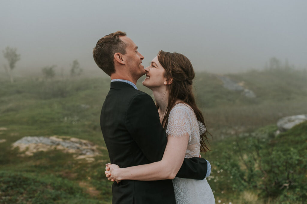 Bride and groom hugging and laughing in front of a foggy landscape