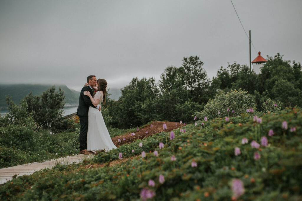 Bride and groom portrait on Senja island with a lighthouse and foggy mountains in the background 