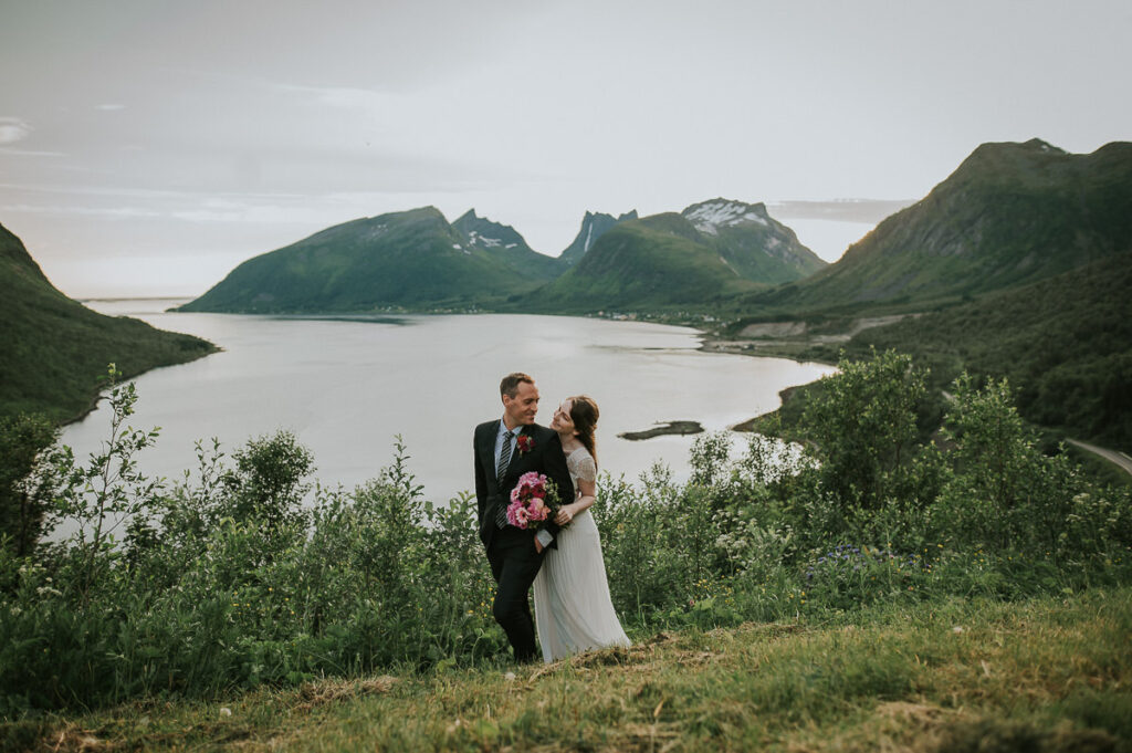 Beautiful bridal couple hugging and smiling to each other on the day of their elopement wedding Senja. Behind them is a gorgeous fjord and mountain view 
