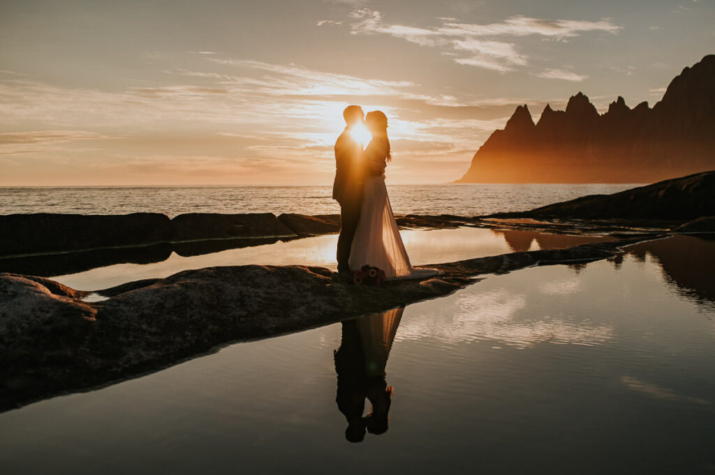Bride and groom kissing on their elopement day in front of spectacular mountains of Senja in the gorgeous midnight sun 
