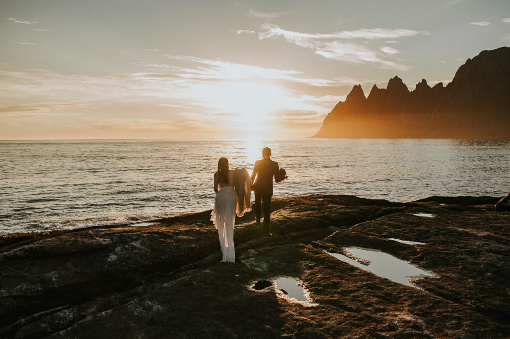 Bride and groom wandering on their elopement day in front of spectacular mountains of Senja in the gorgeous midnight sun 