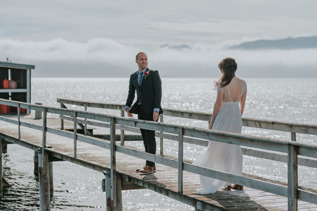 First look on the elopement day where bride walks towards her groom on an old wooden pier in Buvik Sea Lodge outside of Tromsø